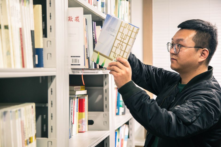 一位国际大一学生在辅导课上与教授交流，背景是图书馆书架
