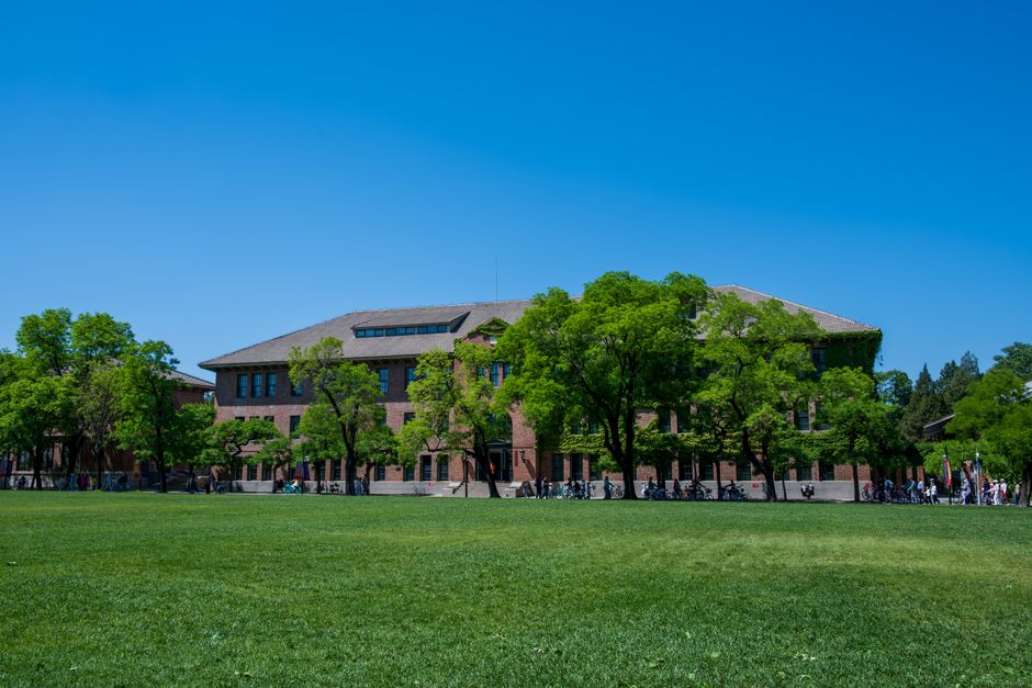 学生群坐在草坪上讨论，背景是古典红砖教学楼
